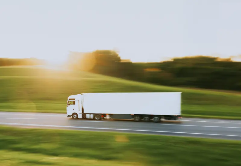 A white freight truck driving along a road at sunset